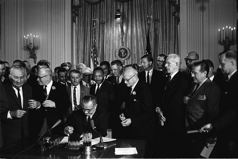 Lyndon B. Johnson promulgă legea drepturilor civile din 1964. Printre invitații aflați în spatele său se numără și Martin Luther King, Jr. - foto preluat de pe ro.wikipedia.org
