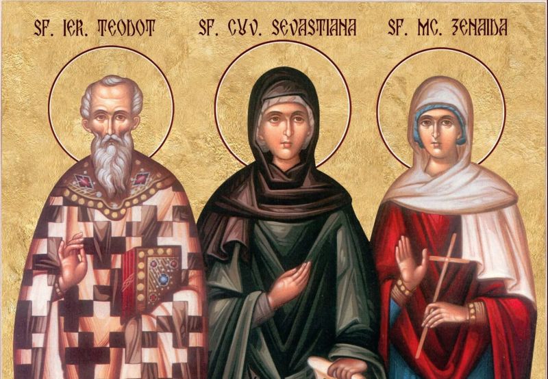 Icoană ortodoxă bizantină pictată în culori calde, înfățișându-i pe Sfântul Ierarh Teodot în veșminte arhierești în centru, flancat de Sfânta Sebastiana și Sfânta Zenaida, toți purtând aureole aurii.