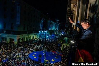 Fotografie de la balconul sediului de campanie, în care Nicușor Dan salută o mulțime entuziastă în noaptea alegerilor, cu un steag mare al Uniunii Europene vizibil în prim-plan, simbolizând victoria forțelor pro-europene.