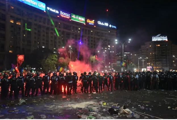 Imagine nocturnă din Piața Victoriei, surprinzând un cordon de jandarmi în fața protestatarilor, în timpul violențelor din 10 august 2018.