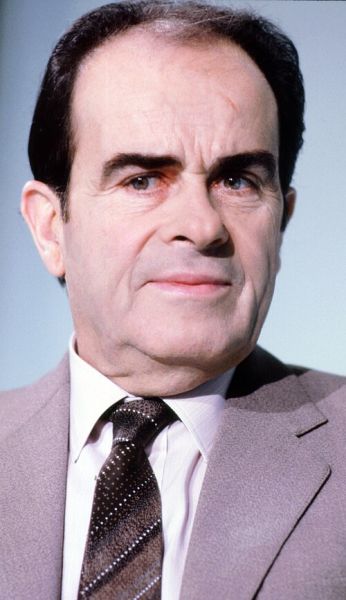Portret fotografic color de tip plan strâns al politicianului Georges Marchais, purtând un costum maro deschis, cămașă cu dungi fine și cravată în nuanțe închise.