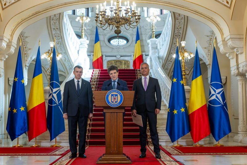 Președintele Nicușor Dan la pupitrul oficial de la Palatul Cotroceni, încadrat de Adrian Veștea și Eugen Tomac, pe fundalul scărilor monumentale și al steagurilor României, UE și NATO.